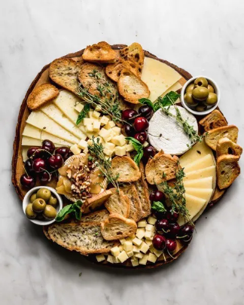 image d'une planche apéro avec du fromage, du pain, des herbes, du raisin et des olives
